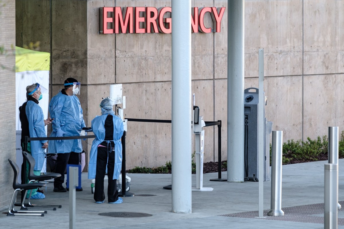 staff in full safety gear stand under a sign that says "emergency"