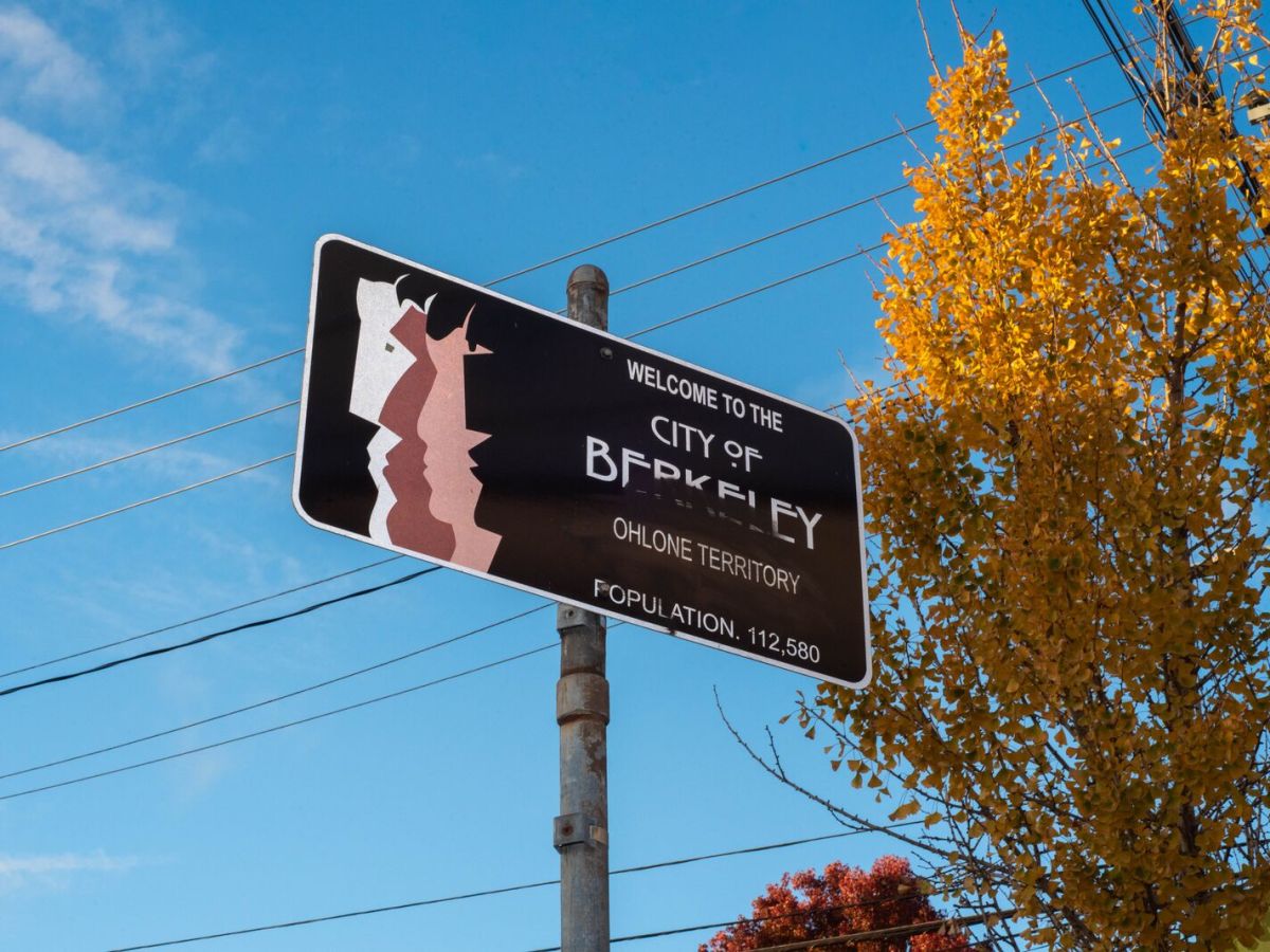 A metal sign reads "welcome to the city of Berkeley, Ohlone territory." It includes the city's logo of four faces in profile.