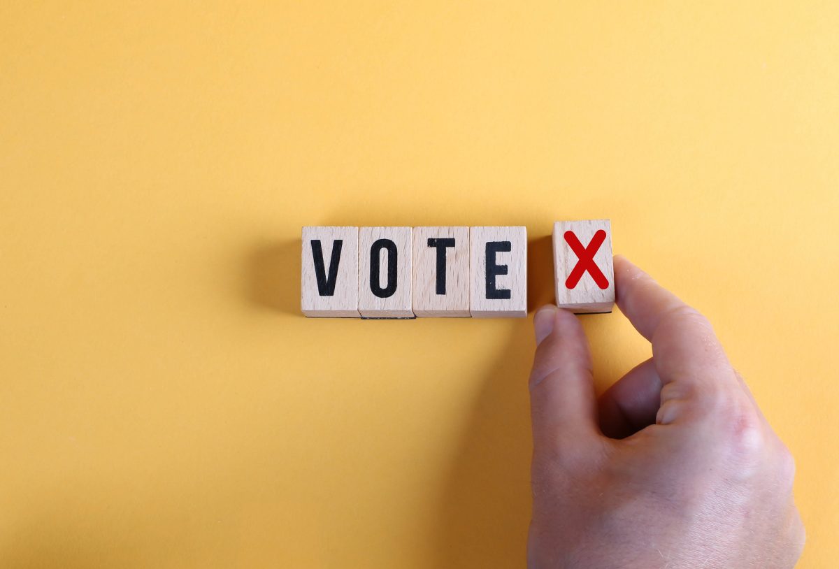 Concept of voting no or negative vote. Male hand placing wooden cube with no symbol next to the cubes with the word vote